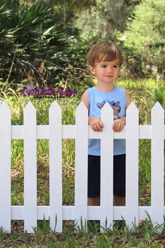 a little boy standing behind a white picket fence