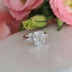 a diamond ring sitting on top of a table next to pink flowers and peonies