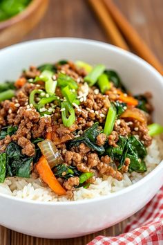 a white bowl filled with rice, meat and veggies next to chopsticks