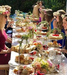 a group of women standing around a table filled with food and drinks, all wearing flower crowns