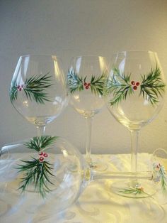 four wine glasses with holly and berries painted on the glass are sitting on a white tablecloth