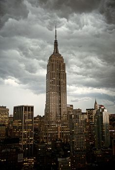 the empire state building towering over new york city at night with storm clouds in the background