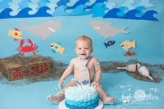 a baby boy sitting on top of a cake with blue frosting and fish decorations