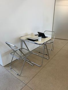 two chairs and a table in front of a white wall with a laptop on it