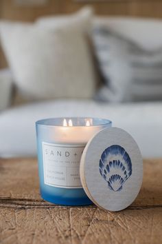 a blue candle sitting on top of a wooden table next to a white bed and pillows