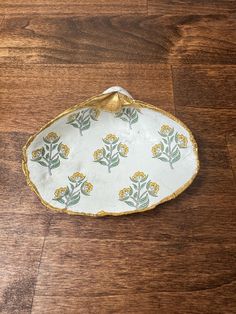 a white and yellow flowered dish on a wooden floor with gold trim around the edge