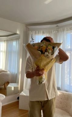 the man is holding flowers in his hands and looking at the camera while standing in front of a window