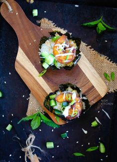 two sushi rolls with cucumbers, tomatoes and other vegetables on a wooden cutting board