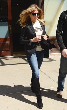 a woman in black jacket and jeans walking down the street with a man behind her