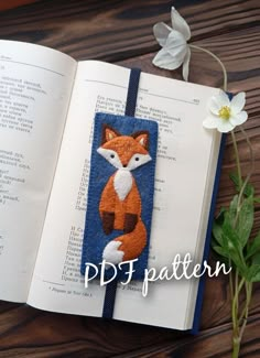 an open book with a fox applique on it next to a white flower