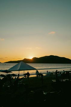 the sun is setting on the beach with people sitting under umbrellas