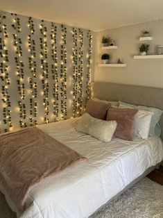 a white bed topped with lots of pillows next to a wall covered in christmas lights