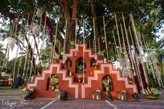 a red and white structure sitting under a tree filled with lots of hanging decorations on it's sides