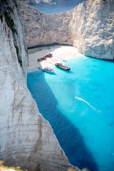 two boats are in the water near some cliffs and blue water with white rocks on either side