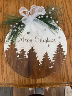 a merry christmas ornament hanging on a wooden table with pine trees and snowflakes