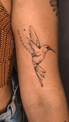 a tattoo on the arm of a woman with a hummingbird flying above her head