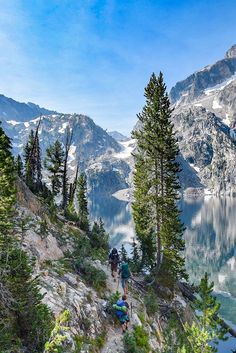 two people hiking up the side of a mountain next to a body of water with mountains in the background