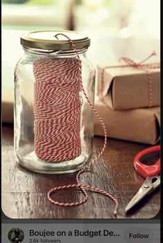 a glass jar with red and white twine in it on a table next to scissors