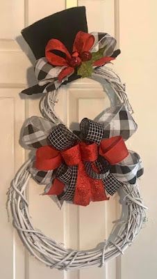 a wreath with red and black bows hanging on the front door, decorated with a top hat