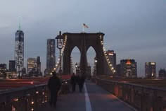 people walking across a bridge at night with the city skyline in the backgroud