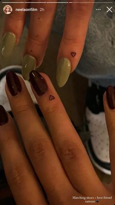 two hands with brown and green nail polishes on their fingers, one has a heart tattoo