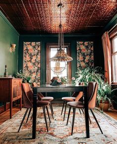 a dining room with green walls and floral wallpaper on the ceiling, along with wooden chairs