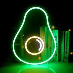 a pear shaped neon light sculpture sitting on top of a table next to bookshelves