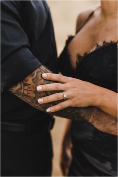 a man and woman holding hands with tattoos on their arms, both wearing black dresses