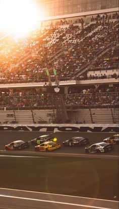 a group of cars driving down a race track in front of a stadium full of people