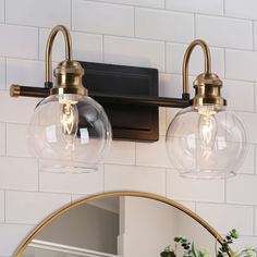 two clear glass globe lights are hanging on the wall above a mirror in a bathroom