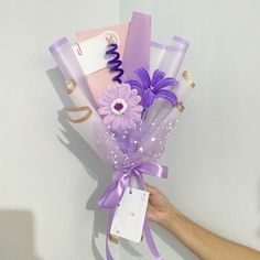 a hand holding a bouquet of flowers with purple ribbons and tags attached to the stems