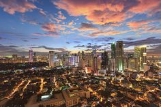 the city skyline is lit up at night with colorful clouds in the sky over it