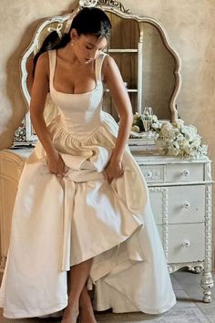 a woman in a white wedding dress standing next to a dresser