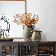 two vases with flowers are sitting on a book shelf in front of a mirror