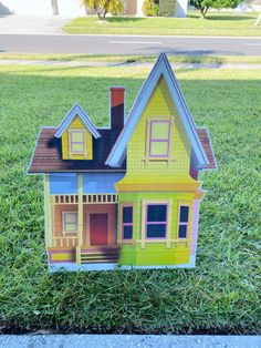 a paper doll house sitting on top of the grass in front of a street sign