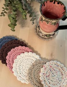 several crocheted coasters sitting on a wooden floor next to a coffee cup