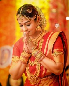 a woman dressed in red and gold with her hands clasped to her chest, praying