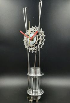 a clock made out of metal with gears on the face and sides, sitting in a glass vase