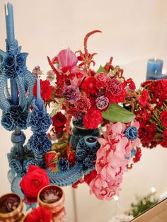 a vase filled with lots of red and blue flowers next to candles on a table