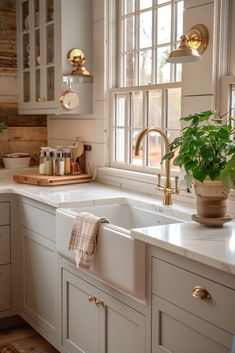 a kitchen with white cabinets and gold fixtures, plants in the window sill next to the sink