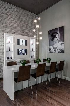 a dining room table and chairs with lights hanging from the ceiling above it, in front of a brick wall