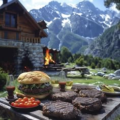 a table topped with hamburgers and other food on top of a wooden table in front of a mountain range