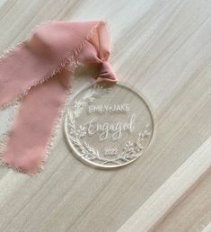 a glass ornament with the name engaged on it next to a pink scarf