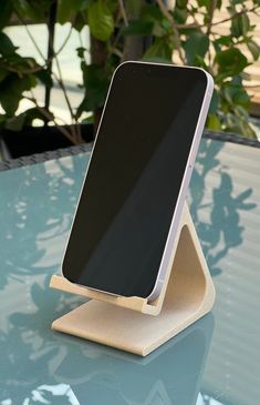 a cell phone sitting on top of a wooden stand in front of a green plant