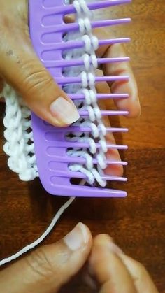 two hands holding a purple comb on top of a wooden table next to a white string