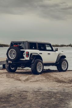 a white jeep parked on top of a sandy beach next to the ocean under a cloudy sky