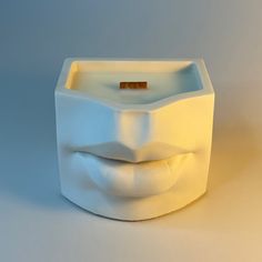 a white square shaped candle holder with a smile on it's face and a wooden stick sticking out of its mouth