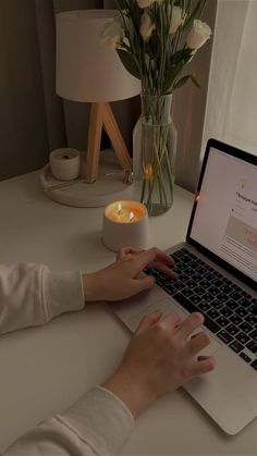 a woman is typing on her laptop at the table with flowers in front of her