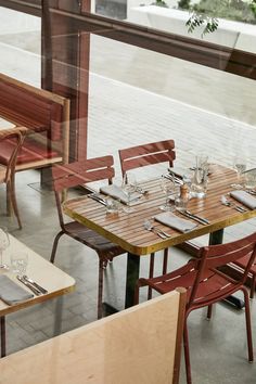 an empty restaurant with wooden tables and red chairs in front of a glass window that looks out onto the street