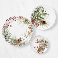 two plates decorated with pine cones, berries and greenery are on a marble surface